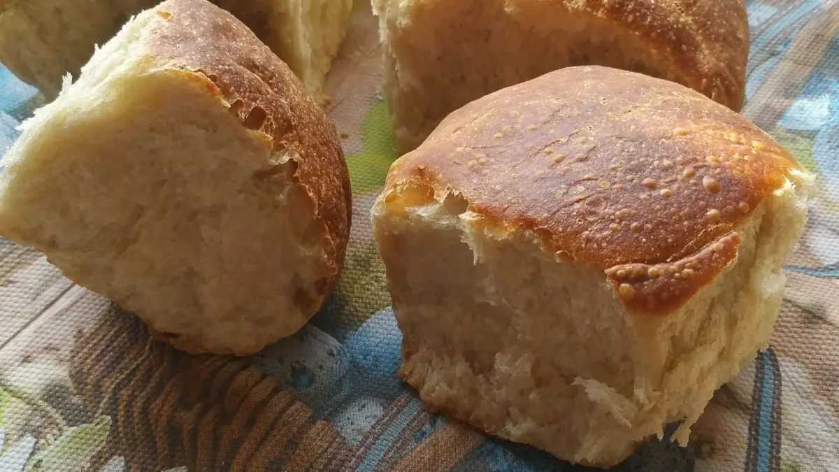 Softe Br&ouml;tchen liegen auf einer bunten Unterlage, frisch gebacken mit goldbrauner Kruste, bereit zum Servieren.