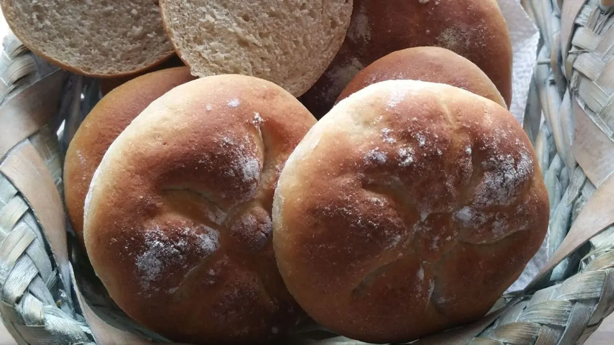 Ein Korb mit frisch gebackenen Dinkel-Buttermilch Br&ouml;tchen liegt auf einem Tisch, einige sind halbiert.