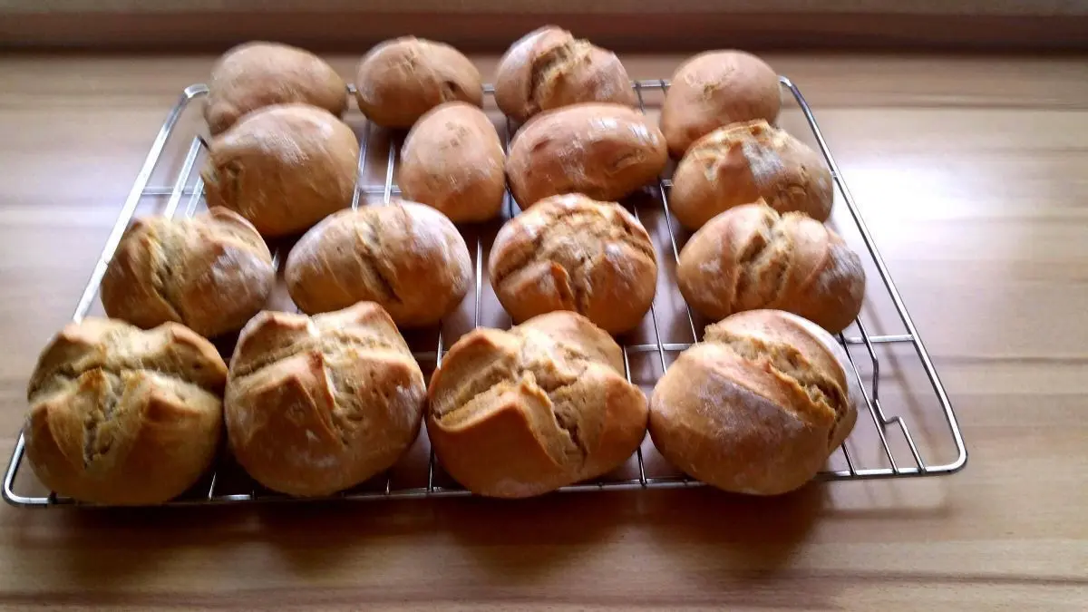 Eine Auswahl frisch gebackener Br&ouml;tchen liegt auf einem Gitter und strahlt mit ihrer zarten Kruste und weichen Krume.