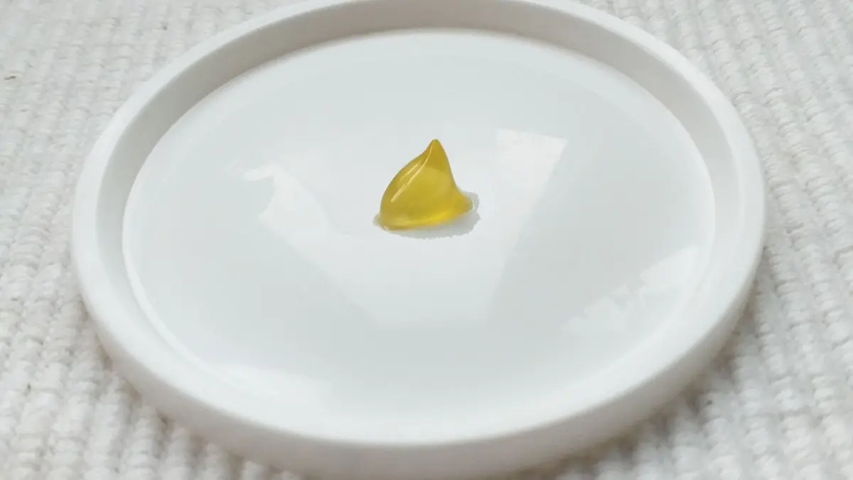Ein kleiner gelbes Heil&ouml;lst&uuml;ckchen liegt in einer wei&szlig;en Schale auf einem weichen, hellen Untergrund.