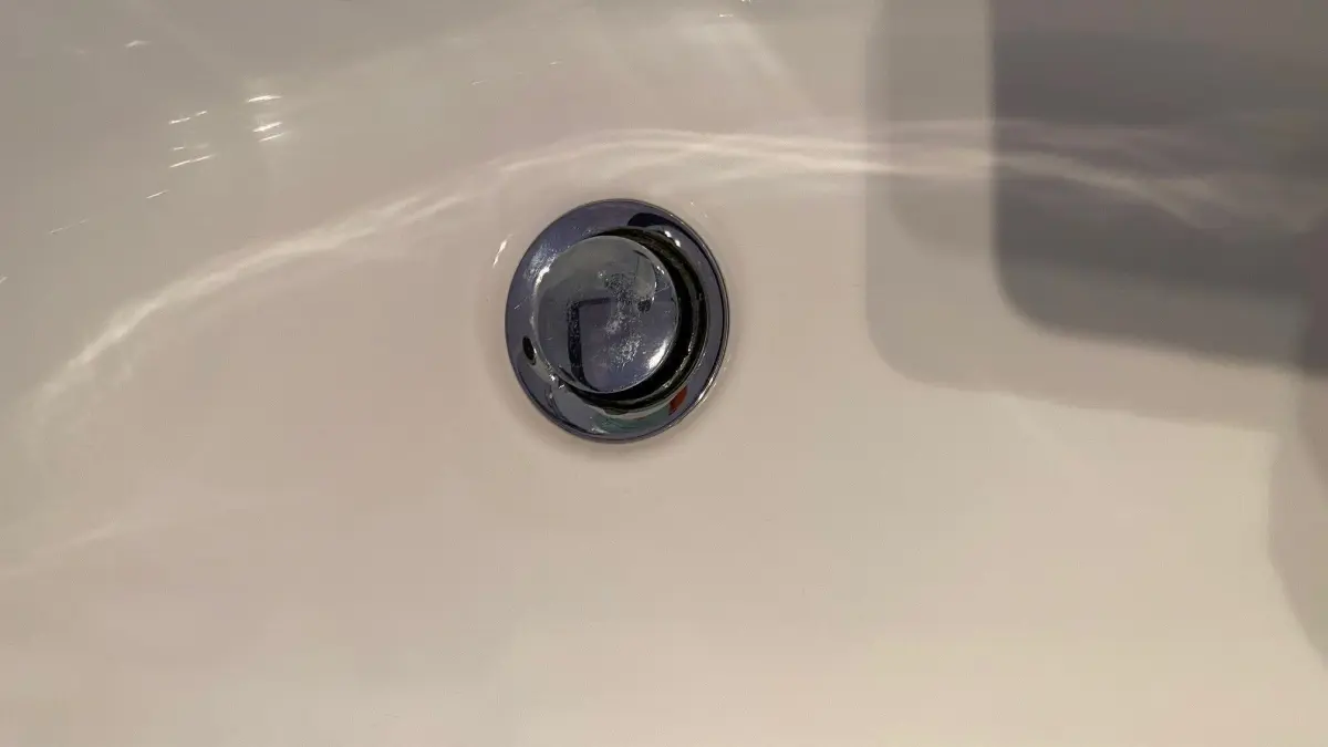 Ein Abflussloch in einer Badewanne zeigt sich in der N&auml;he von glattem, wei&szlig;em Material, das Wasser abf&uuml;hren soll.