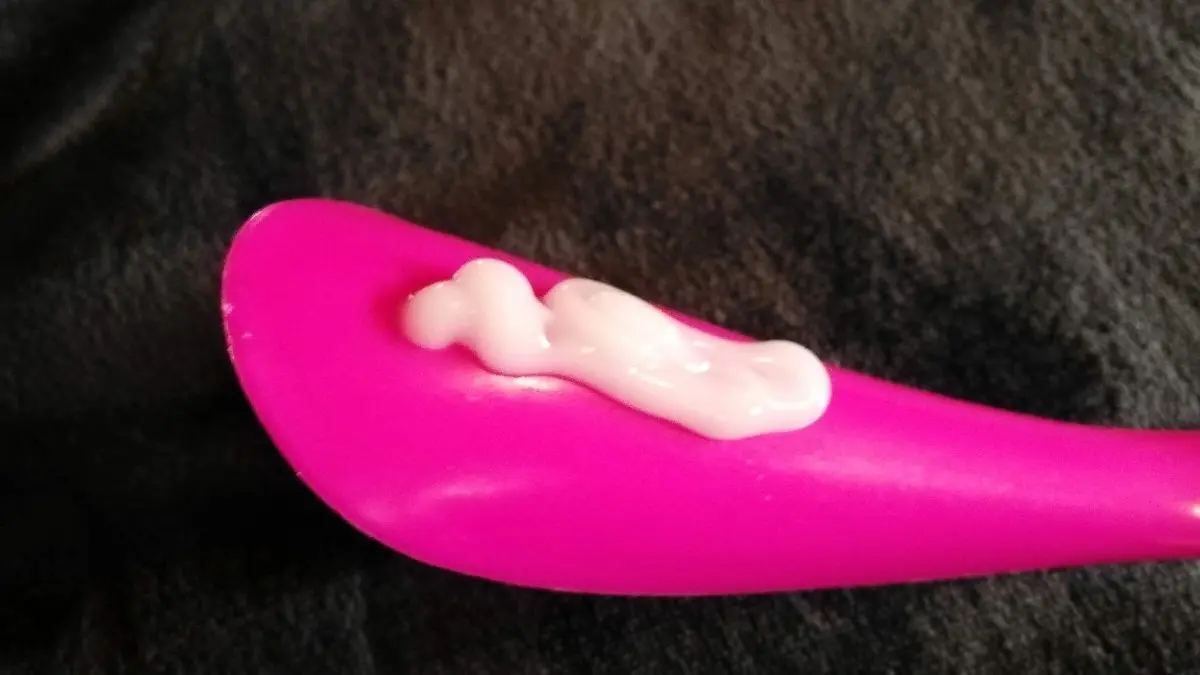 Ein pinker Ausstrichhilfe ist mit Lotion gef&uuml;llt und liegt auf einem dunklen Tuch, bereit f&uuml;r das Eincremen des R&uuml;ckens.