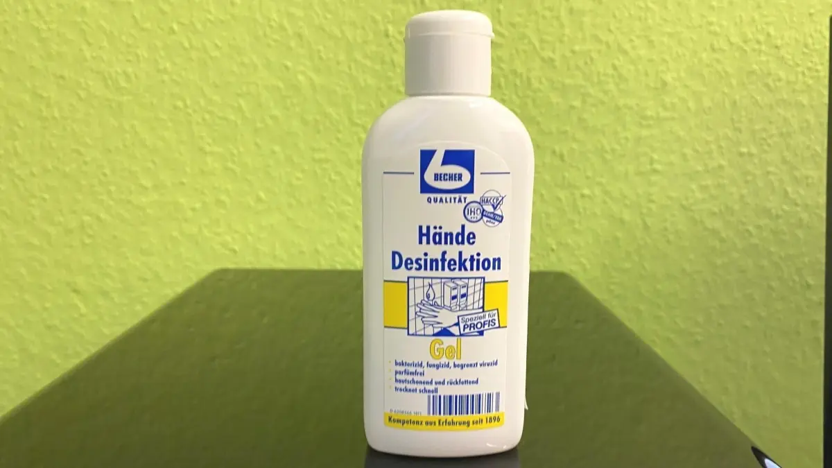 Eine Flasche mit Desinfektionsmittel steht auf einem Tisch vor einer gr&uuml;nen Wand und zeigt die Aufschrift "H&auml;nde Desinfektionsmittel".