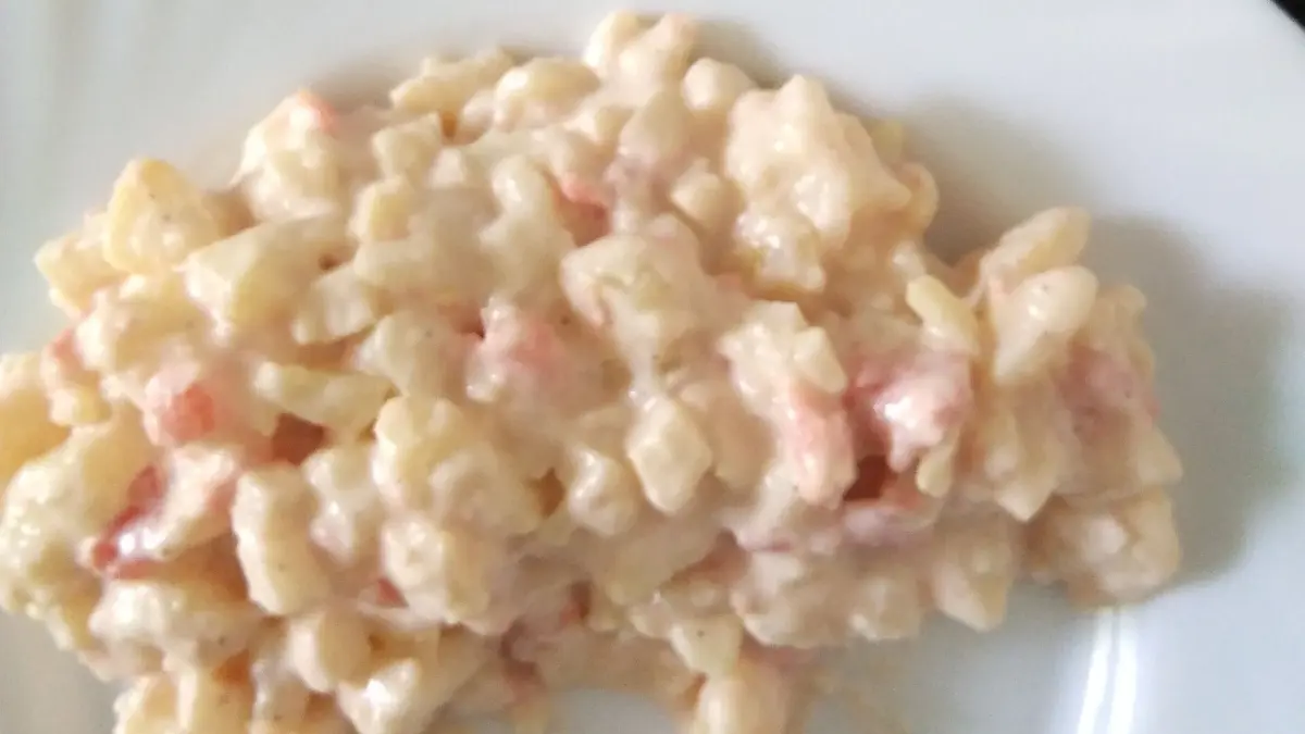 Ein cremiger Kartoffelsalat mit kleinen St&uuml;cken, der auf einem wei&szlig;en Teller angerichtet ist, wirkt einladend und frisch.