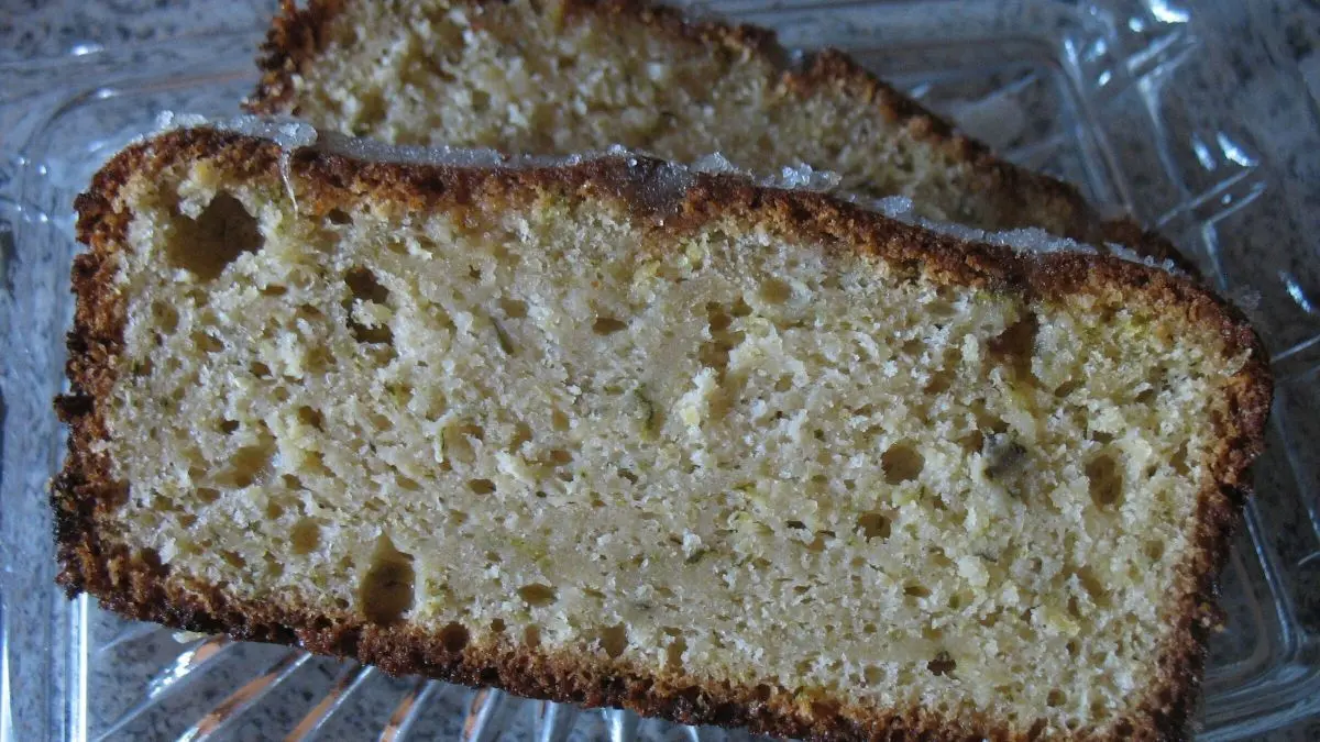 Zwei saftige St&uuml;cke Zucchini-Zitronen-Kuchen liegen auf einem transparenten Teller, umgeben von einer hellen, neutralen Umgebung.