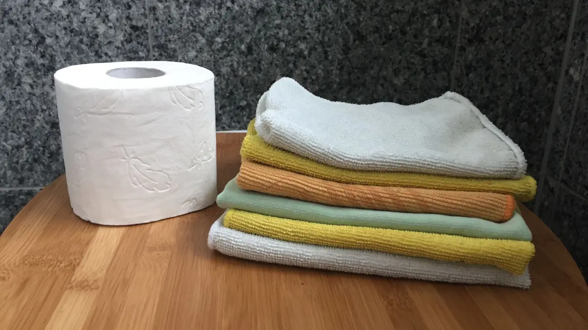 Ein Rollen Klopapier steht neben einem Stapel handt&uuml;cher in einem modernen, hellen K&uuml;chenumfeld auf einem Holzbrett.