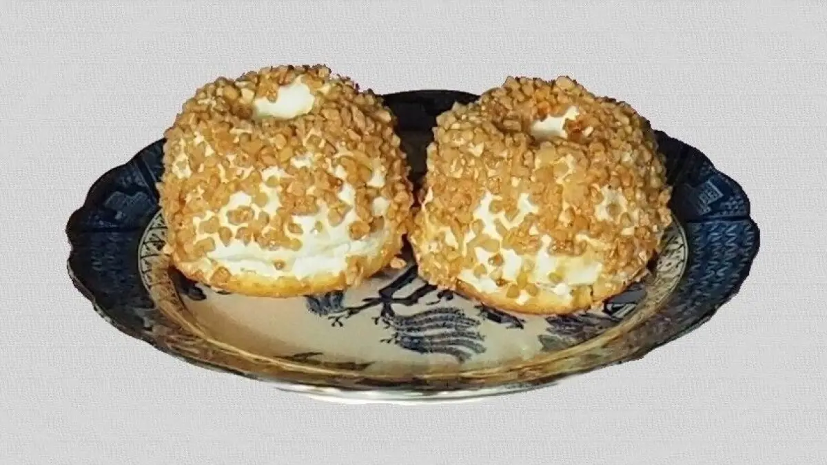 Zwei k&ouml;stliche, mit Buttercreme gef&uuml;llte Geb&auml;ckst&uuml;cke liegen auf einem dekorativen Teller mit goldenen Kanten.