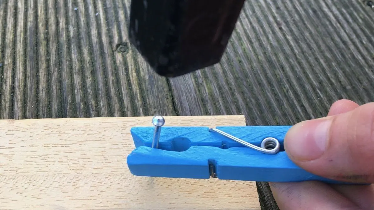 Ein blauer Nagelhalter wird benutzt, um einen Nagel pr&auml;zise in ein Holzbrett zu schlagen, ohne blaue Finger zu bekommen.