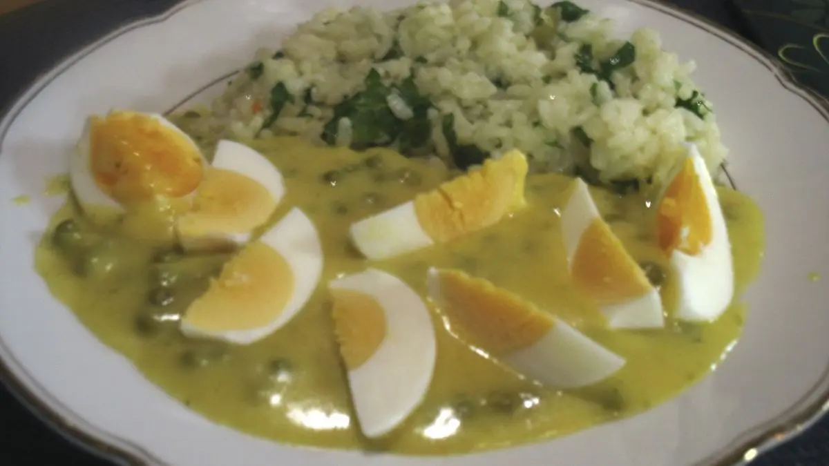 Butter-Kr&auml;uter-Reis wird neben einer Currysauce und in Scheiben geschnittenem Ei auf einem Teller serviert.