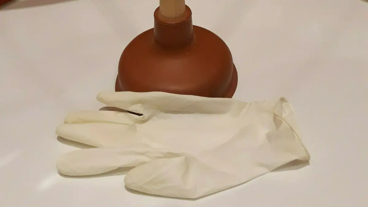 Ein P&uuml;mpel steht neben wei&szlig;en Handschuhen auf einer hellen Oberfl&auml;che, bereit zur chemiefreien Abflussreinigung.