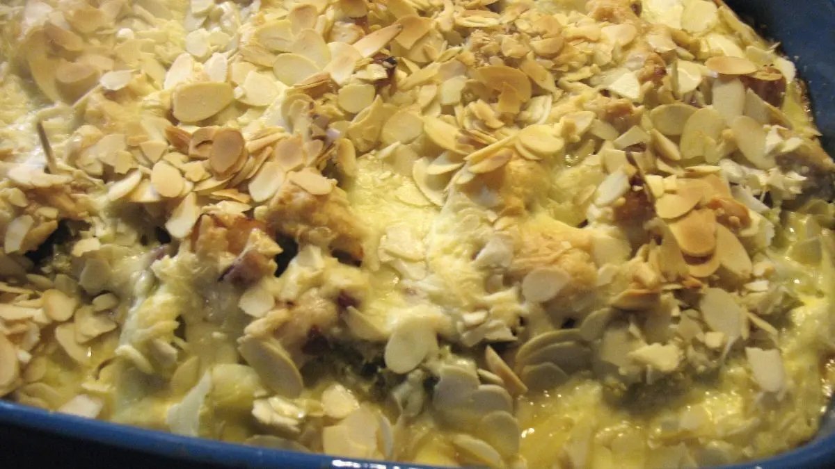 Sahniges Brokkoli-Kartoffel-Gratin mit H&auml;hnchenbrust ist goldbraun, &uuml;berbacken mit Mandelsplittern in einer blauen Auflaufform.