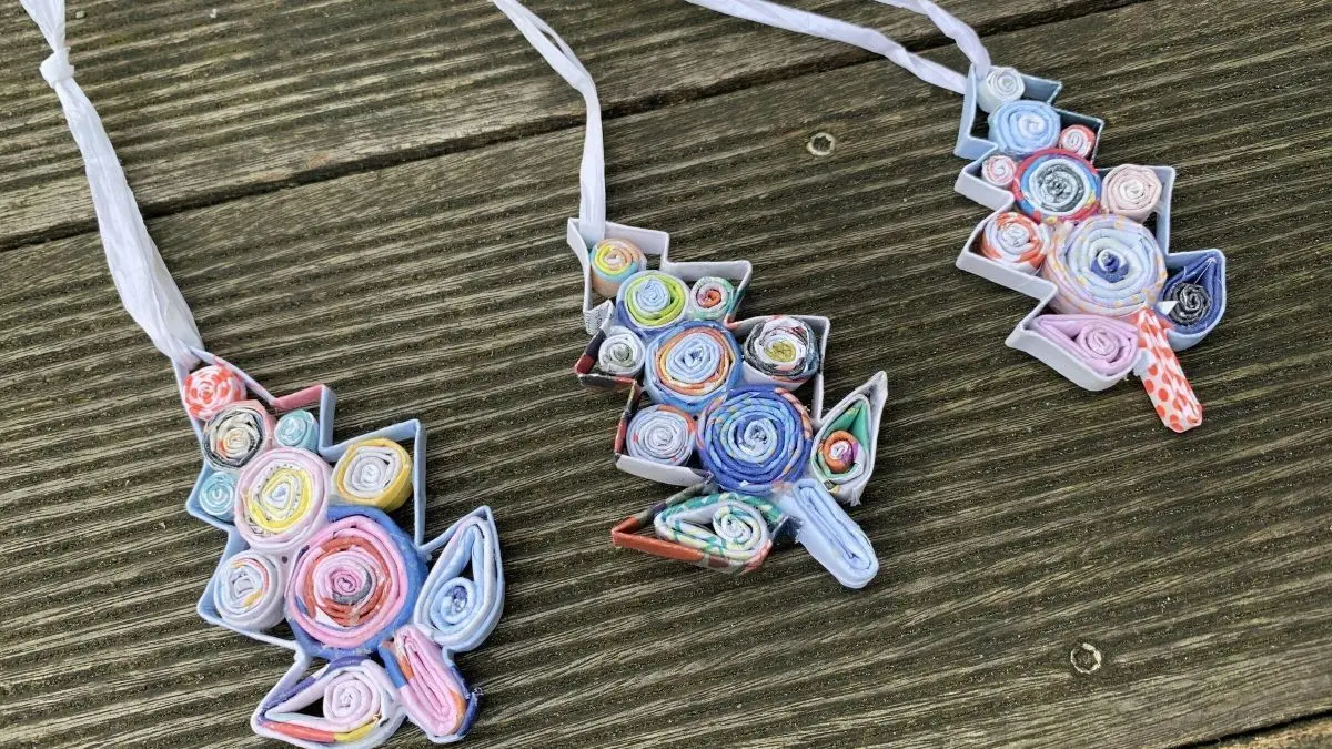 Bunte Tannenbaumschmuck aus Altpapier h&auml;ngt an F&auml;den, auf einer Holzoberfl&auml;che platziert, ideal f&uuml;r DIY Recycling.