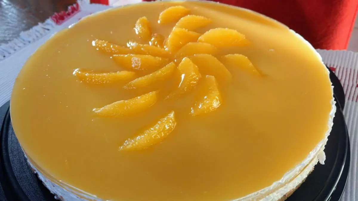 Die Orangentorte mit Spekulatiusboden steht auf einem runden Teller, garniert mit Orangenscheiben und gl&auml;nzender Glasur.