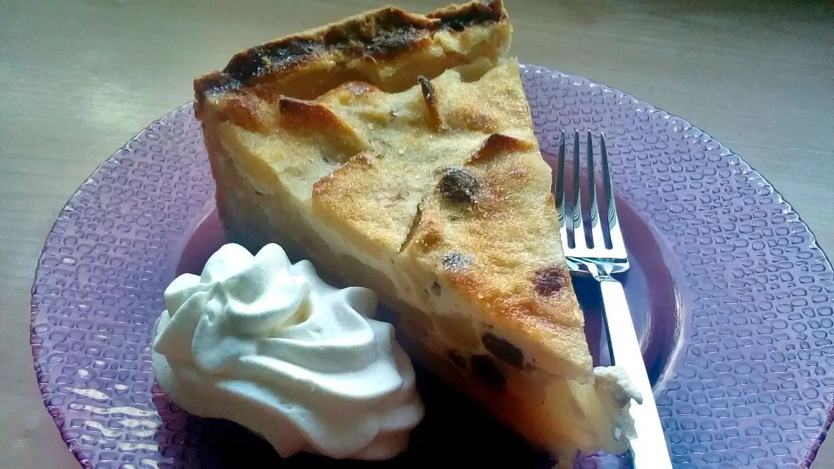 Ein St&uuml;ck K&auml;se-Apfel-Kuchen liegt auf einem lila Teller, neben einem Klecks Sahne und einer Gabel.