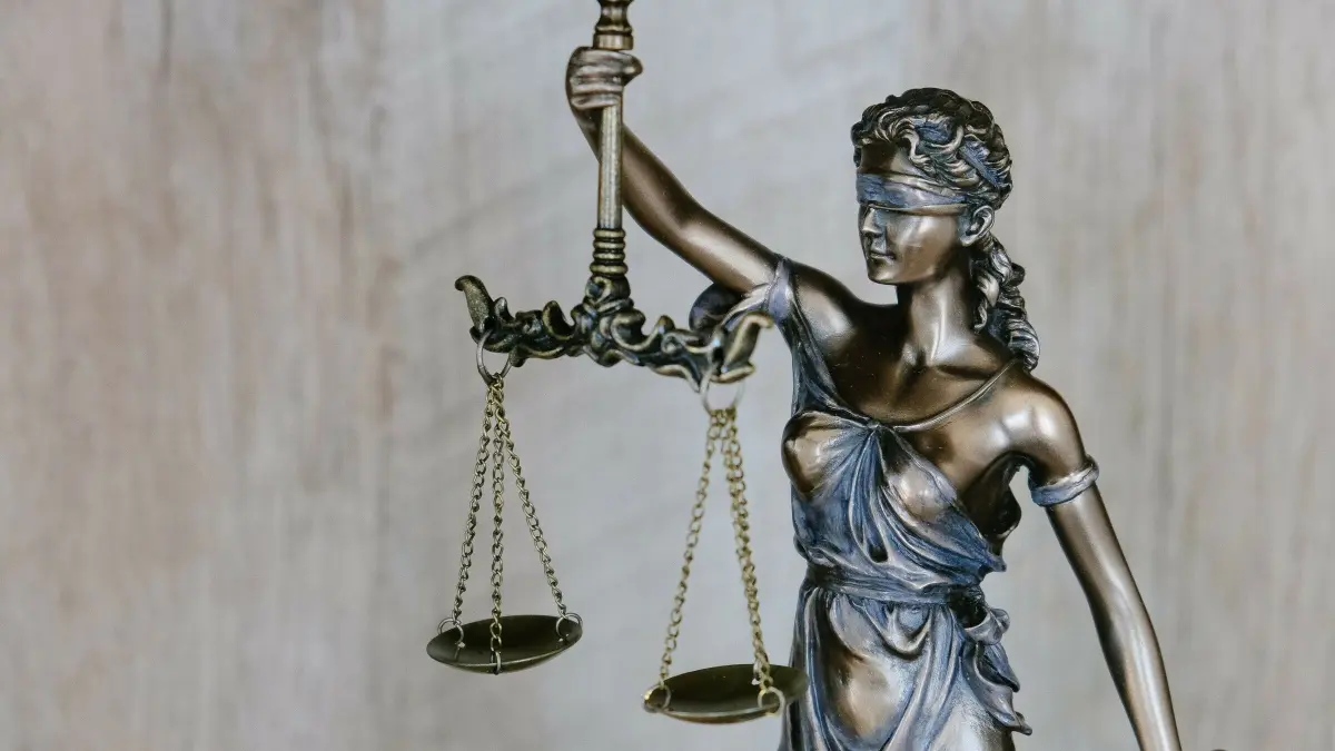 Eine Statue der Justitia h&auml;lt in einer Hand eine Waage, symbolisch f&uuml;r Gerechtigkeit, vor einem neutralen Hintergrund.