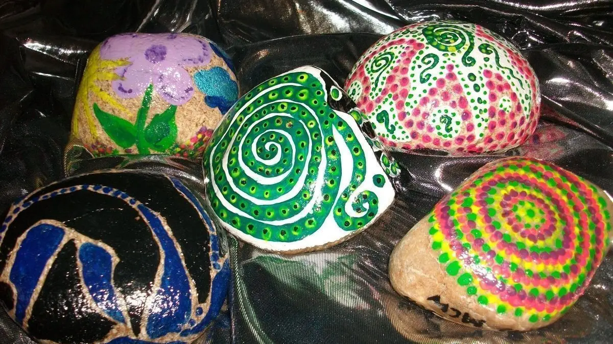 Bunte bemalte Steine liegen auf einem glitzernden Stoff, jede mit einzigartigen Mustern und Farben gestaltet.