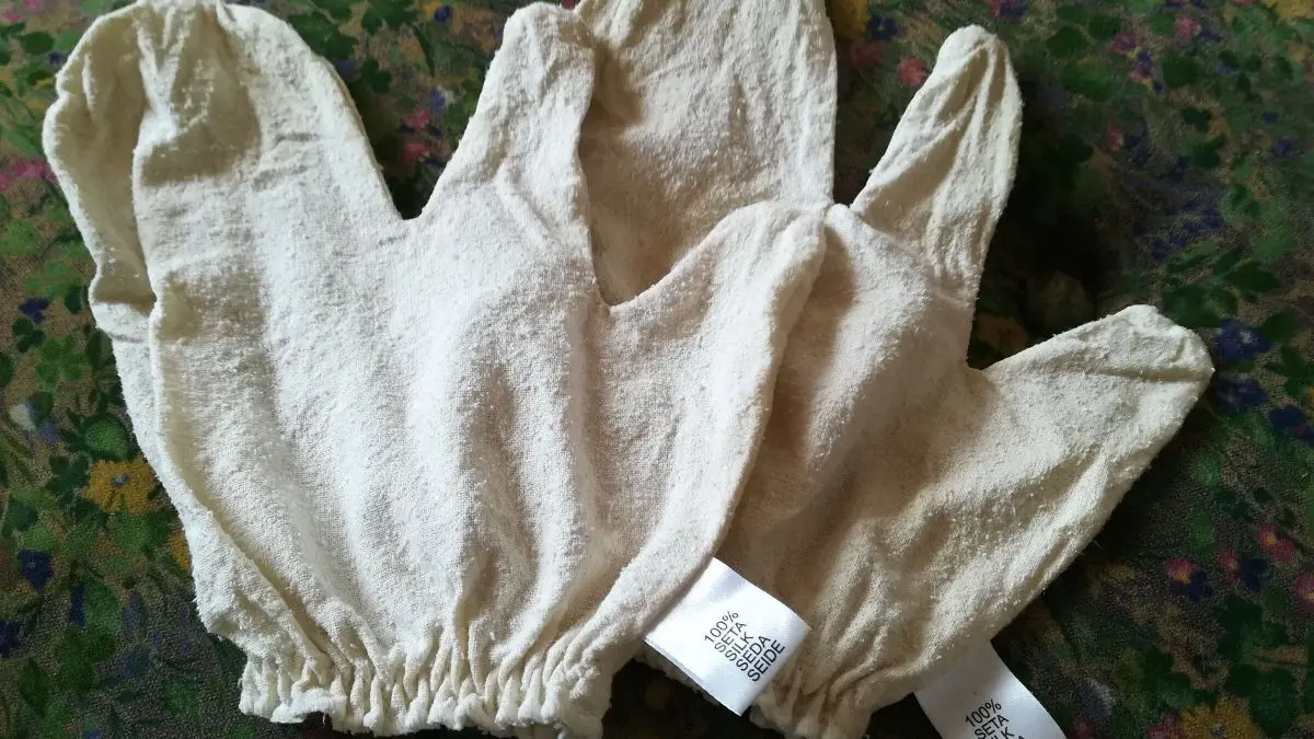 Seidenhandschuhe liegen auf einem bunten Stoff, bereit f&uuml;r eine Massage zur Anregung des Stoffwechsels.