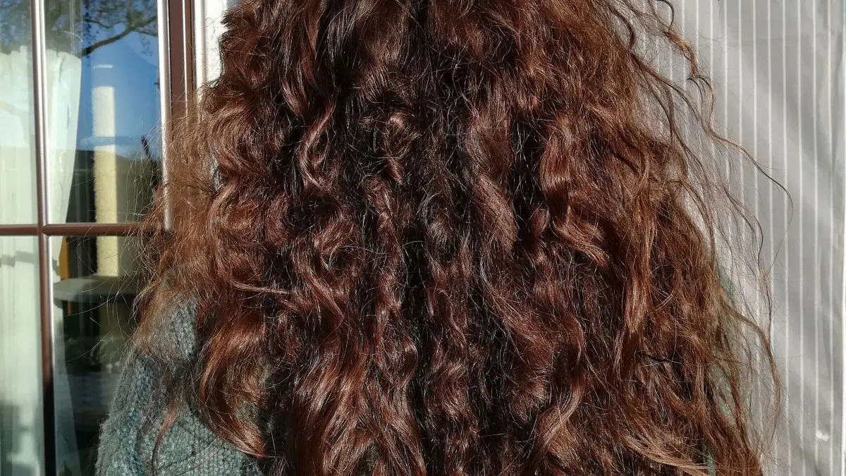 Lange, lockige Haare fallen auf die Schultern einer Person, die drau&szlig;en steht, im warmen Sonnenlicht.