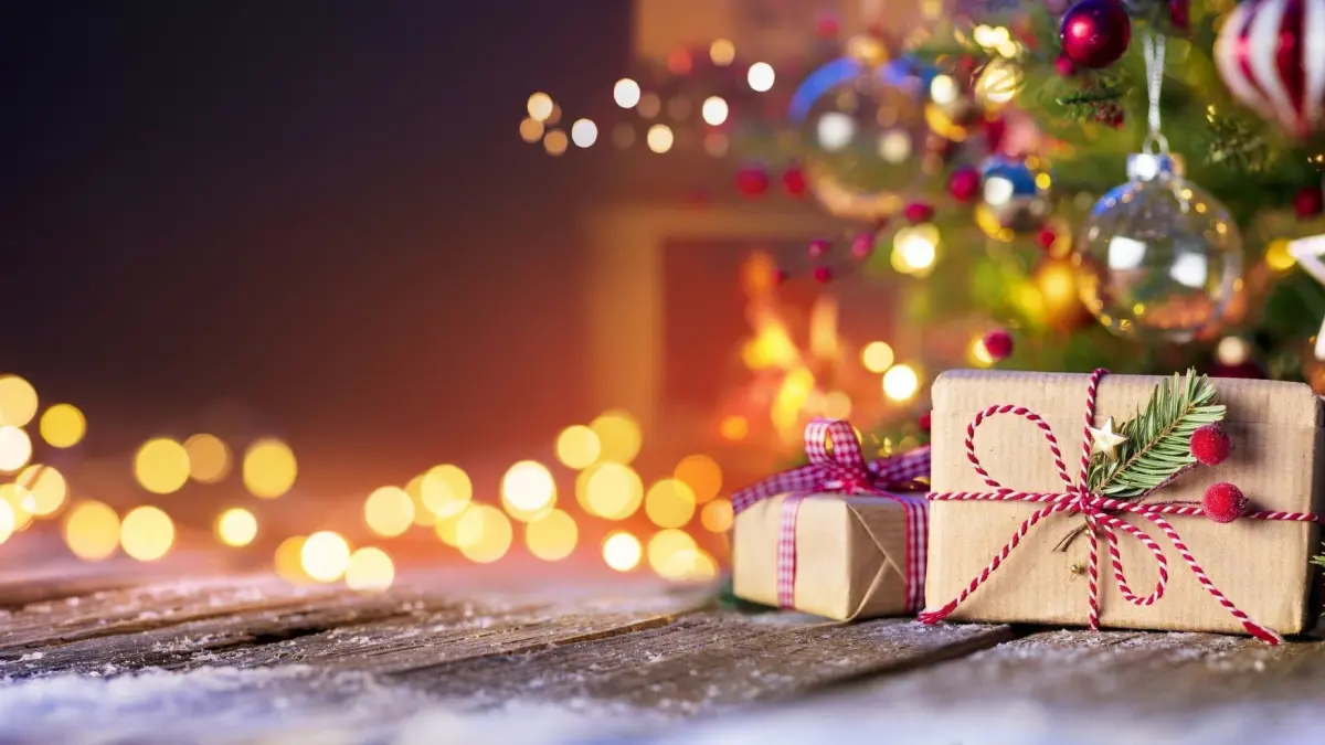 Festlich dekorierte Geschenke liegen auf einem Holztablett, umgeben von einem Weihnachtsbaum und warmen Lichtern.