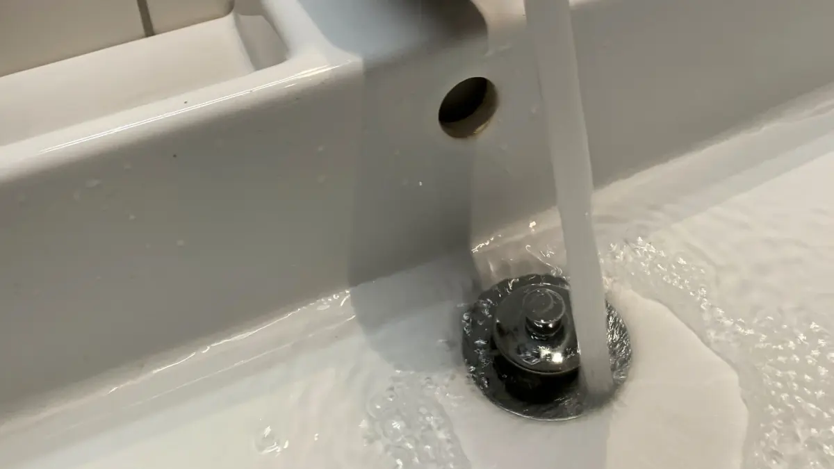 Ein gl&auml;nzender Wasserhahn l&auml;sst Wasser in ein Waschbecken laufen, w&auml;hrend die flie&szlig;ende Str&ouml;mung auf der Wasseroberfl&auml;che spritzt.