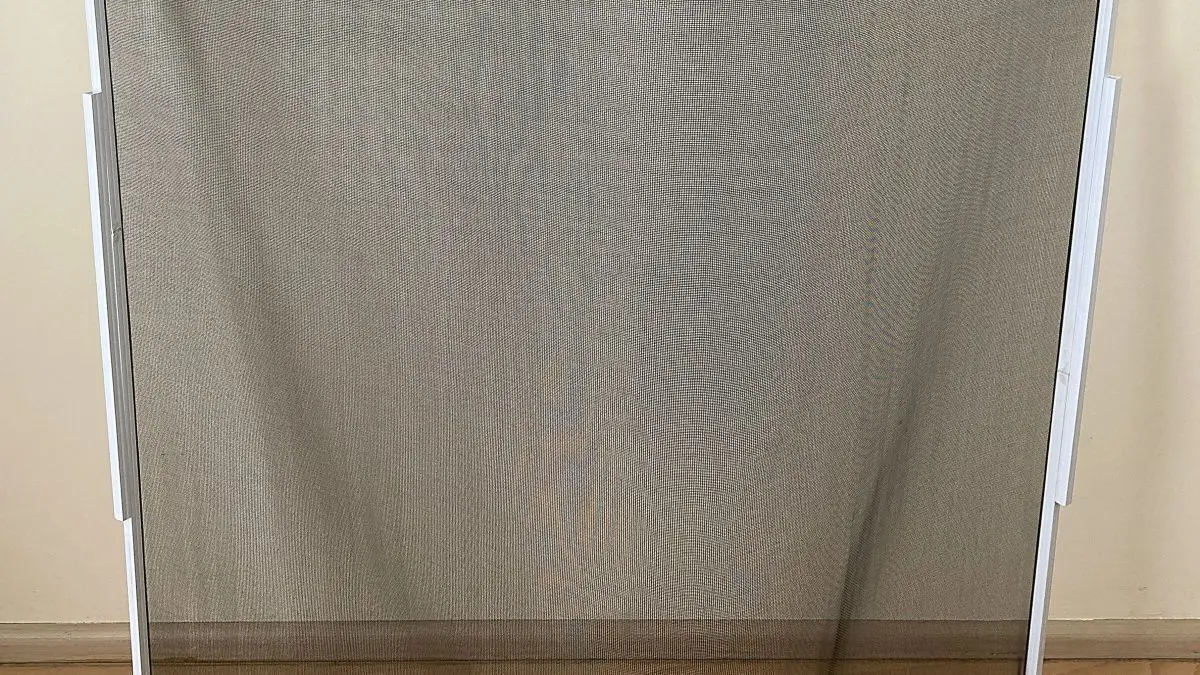 Ein zusammenklappbares Fliegengitter steht gefaltet auf einem Holzboden und sch&uuml;tzt vor Insekten im Raum.