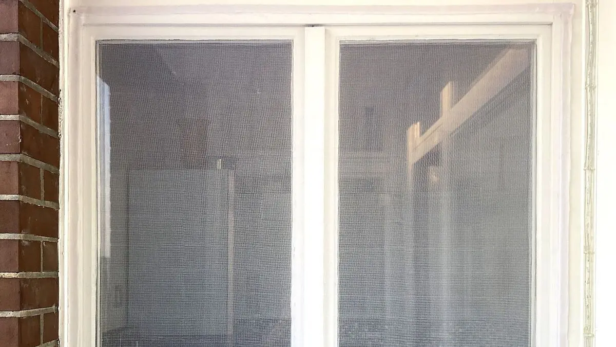 Ein flexibles Fliegengitter wird an einem wei&szlig;en Fenster montiert, um Insekten drau&szlig;en zu halten. Das Fenster ist in ein modernes Wohnumfeld integriert.