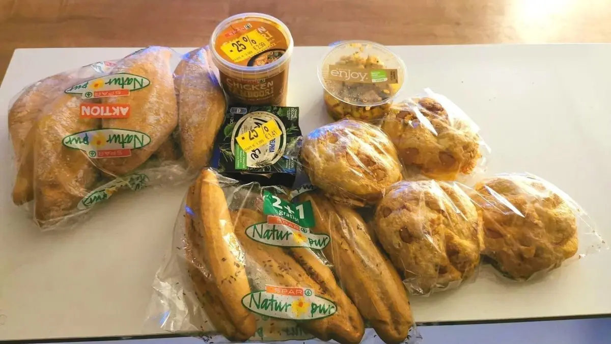 Auf einem Tisch liegen verpackte Lebensmittel: Br&ouml;tchen, Bananen und Dips. Eine Aktion des Lebensmittelrettens verdeutlicht den Kontext der Verwertung.