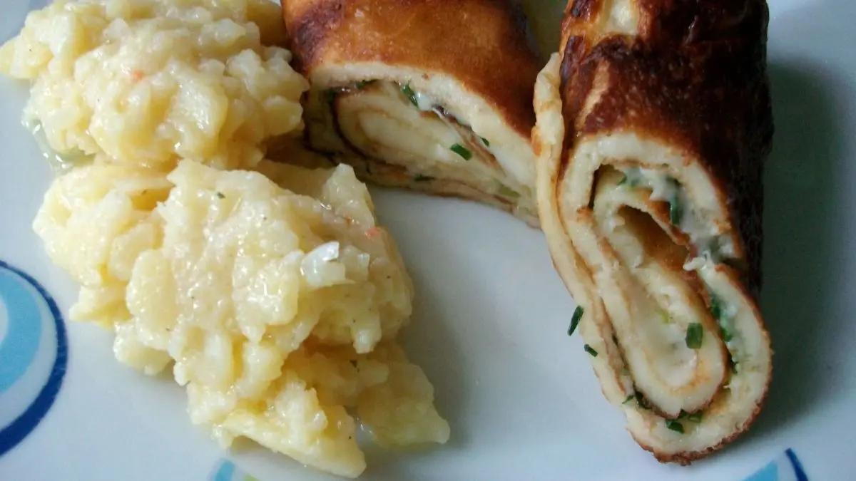 Dinkel-Pfannkuchen sind auf einem Teller angerichtet, gef&uuml;llt mit K&auml;se und Schnittlauch, daneben eine Portion Kartoffelbrei.
