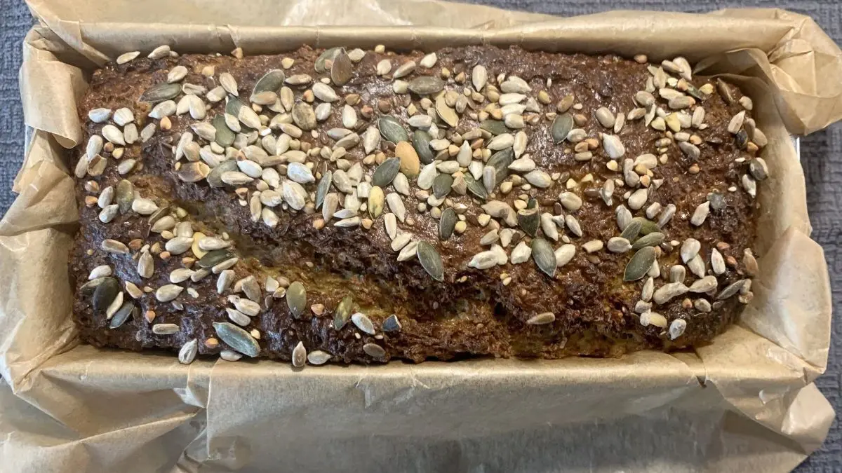 Ein frisch gebackenes Low Carb Eiwei&szlig;brot mit Chiasamen und unterschiedlichen Samen auf der Oberfl&auml;che liegt in einer Backform.