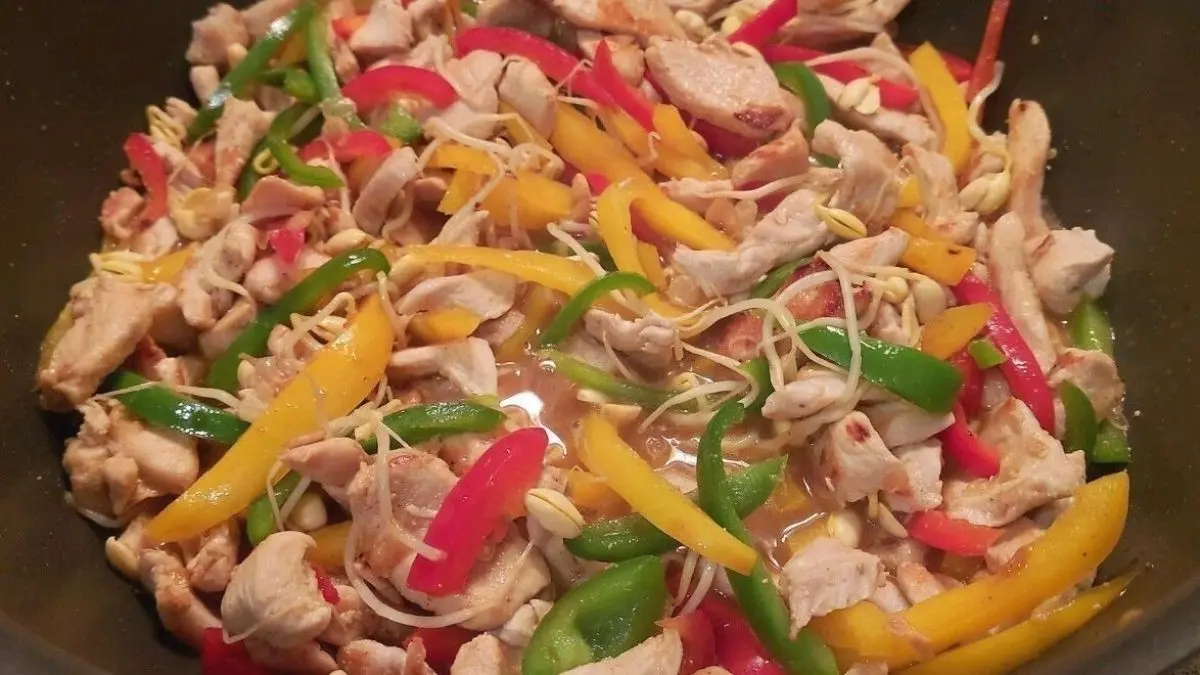 Bunte asiatische Gem&uuml;sepfanne mit H&auml;hnchenst&uuml;cken wird in einer Sch&uuml;ssel angerichtet und dampft appetitlich.