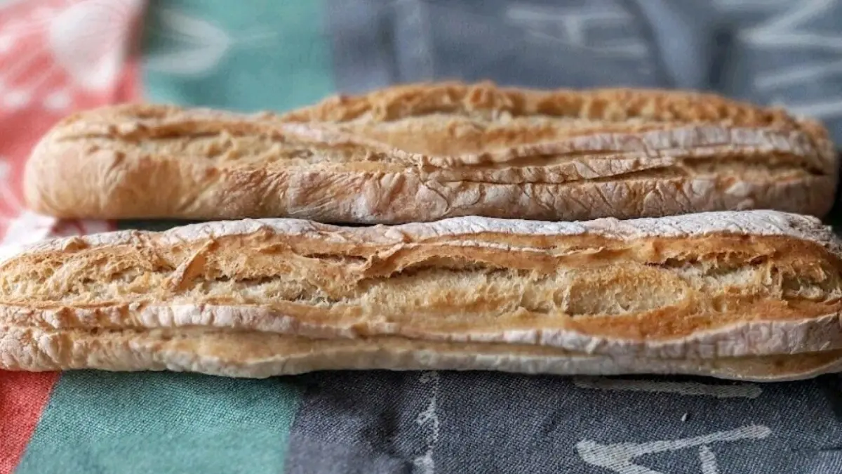 Zwei frisch gebackene Dinkelbaguettes liegen auf einem bunten Geschirrtuch und warten darauf, serviert zu werden.