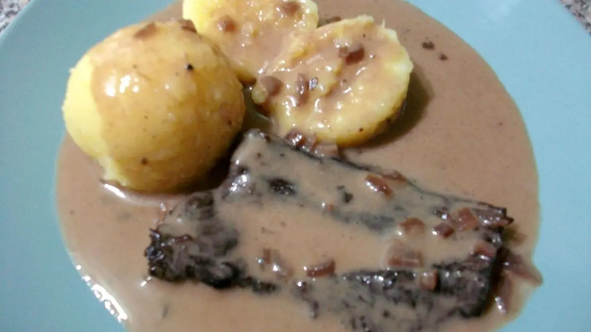 Ein zartes Rindersteak liegt in einer cremigen Rotwein-Sahneso&szlig;e, umgeben von Kartoffelkn&ouml;deln auf einem blauen Teller.