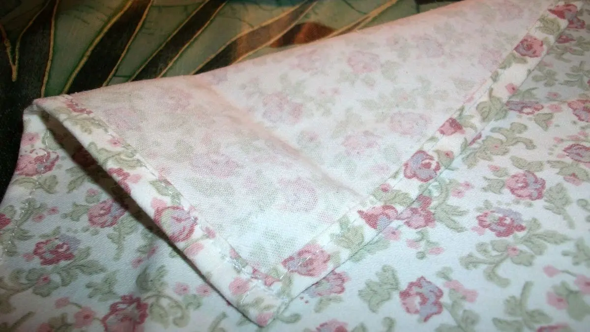 Ein h&uuml;bsch gen&auml;htes Geschirrtuch aus alter Bettw&auml;sche zeigt florale Muster und klare N&auml;hte, umweltbewusste Handarbeit.