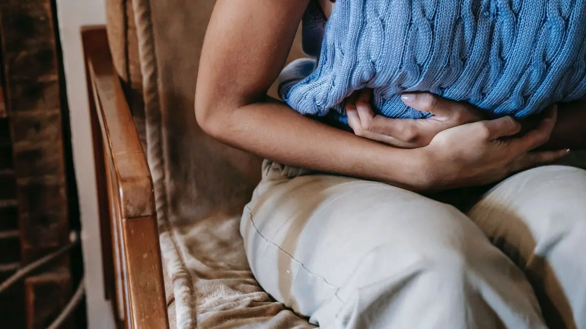 Ein Mensch sitzt auf einer Couch, umarmt einen blauen Kissen, w&auml;hrend er sich schmerzhafte Perioden lindert.