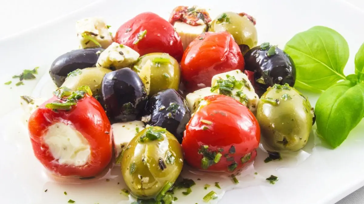 Bunter Antipasti-Salat mit Tomaten, Oliven und Feta, mariniert in Kr&auml;uter&ouml;l, auf einem wei&szlig;en Teller angerichtet.