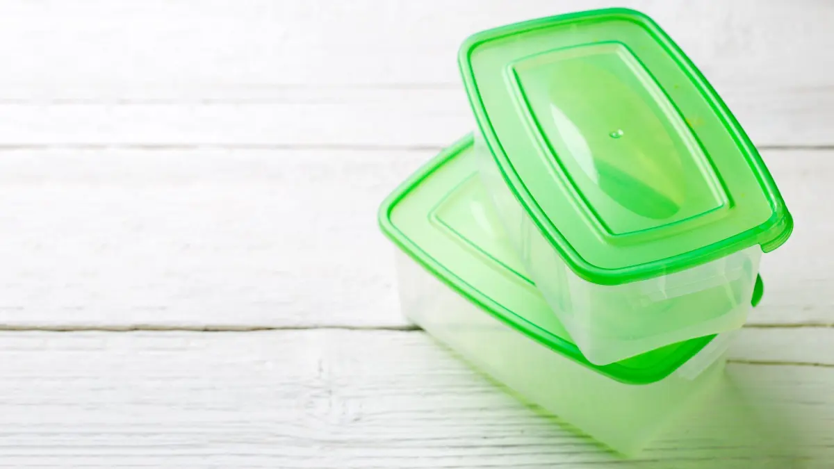 Transparente Tupperware mit gr&uuml;nen Deckeln steht auf einem hellen Holztisch, bereit zur Reinigung von Verf&auml;rbungen.