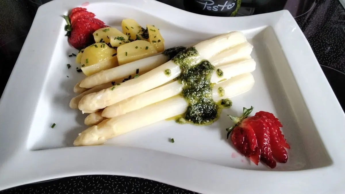 Wei&szlig;er Spargel liegt auf einem Teller, garniert mit B&auml;rlauch-Pesto, dazu Kartoffeln und Erdbeeren. Frisch und ansprechend.