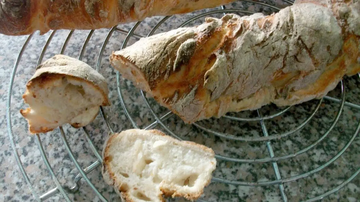 Wurzelbrot liegt auf einem Gitter zum Abk&uuml;hlen, mit einem aufgeschnittenen St&uuml;ck, das die fluffige Textur zeigt.