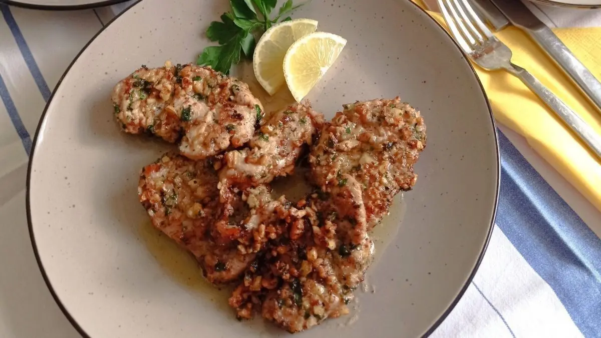 Putenschnitzel liegen auf einem Teller mit Walnusskruste und sind mit Zitronenscheiben und Petersilie garniert, umgeben von frischem Salat.