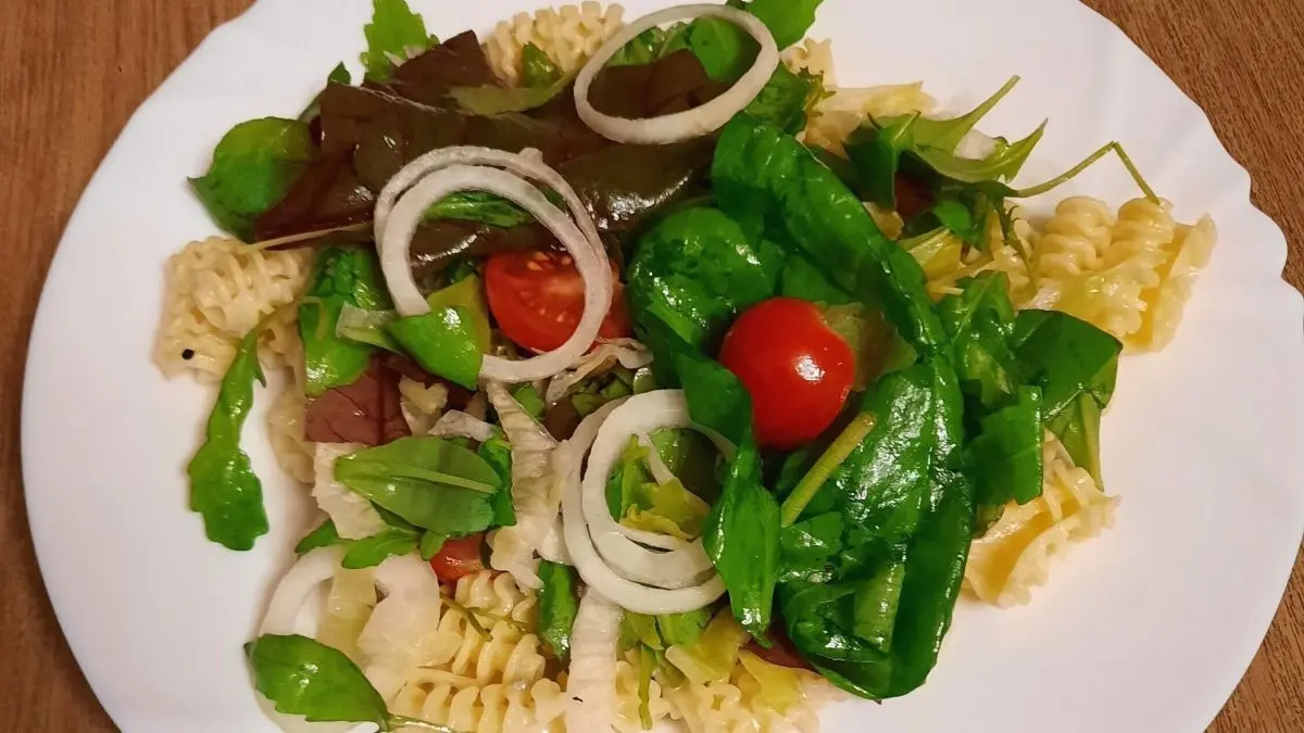 Eine Portion Gorgonzolanudeln wird mit frischem Babyspinat und Tomaten auf einem wei&szlig;en Teller serviert, umgeben von Holz.