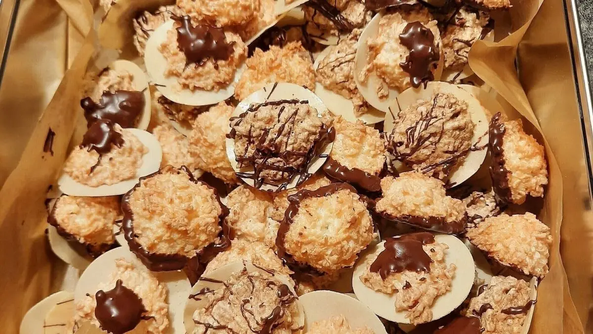 Kokosmakronen, sowohl mit als auch ohne Schokoglasur, liegen ordentlich in einer Blechdose auf braunem Papier.