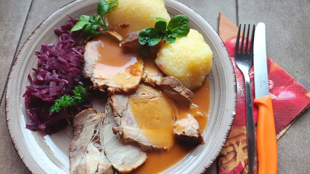 Zart geschnittenes Salzbraten mit Honig-Senf-Kruste auf einem Teller, umgeben von Rotkraut und knusprigen Kn&ouml;deln.