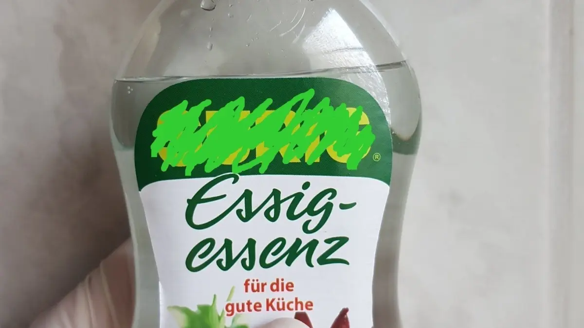 Eine Hand h&auml;lt eine Flasche Essig-Essenz, die f&uuml;r die K&uuml;che mit Gem&uuml;seillustrationen auf dem Etikett beschrieben wird.