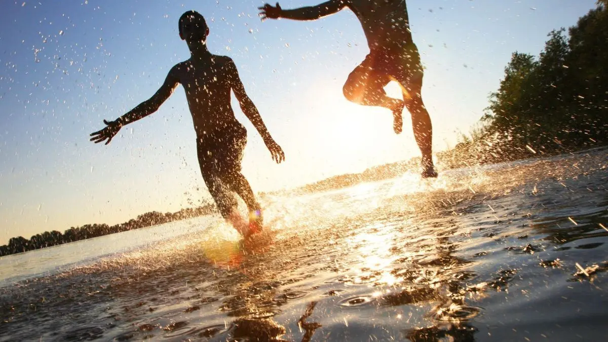 Zwei Kinder springen fr&ouml;hlich ins Wasser, w&auml;hrend die Sonne untergeht, und verspr&uuml;hen dabei spritzige Wassertropfen im Sommerurlaub.