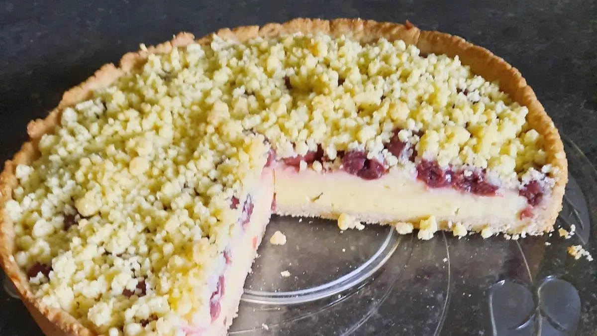 S&uuml;&szlig;er Kirsch-Streuselkuchen mit einer goldenen Kruste und einer schmalen Schnittkante auf einem eleganten Glassicht.
