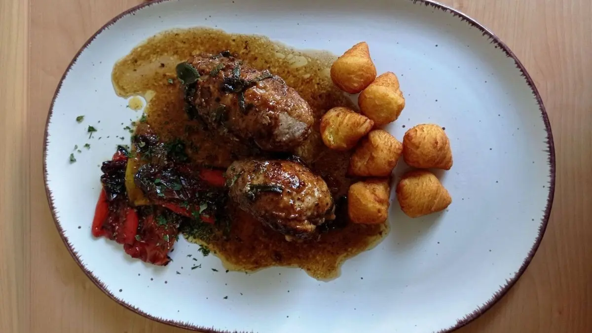 Kalbfleischrouladen sind mit Parmaschinken und Salbei serviert, begleitet von R&ouml;stkartoffeln und Gem&uuml;se auf einem wei&szlig;en Teller.