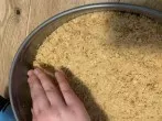 Die Butter-Keksbr&ouml;sel-Masse in eine eingefettete Springform geben und zu einem Boden andr&uuml;cken. Dabei kann man auch einen kleinen Rand formen. 