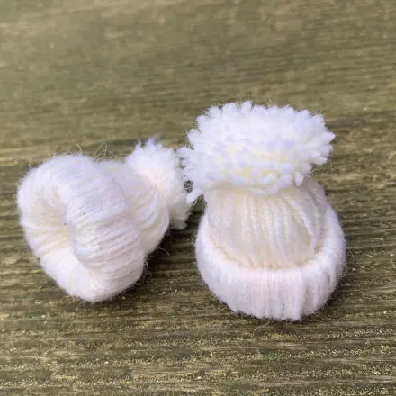 Hier sieht man zwei kleine fertig gebastelte Mini-Mützchen aus Wolle.
