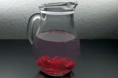 Aromatisiertes Wasser: Zerdr&uuml;ckte Himbeeren in einen Krug mit Wasser