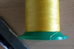 Damit sich das Garn bei Nichtverwendung nicht nach und nach von der Kone abwickelt, schneide ich immer vor Gebrauch eine Kerbe in den unteren Rand und klemme den Faden hier ein.